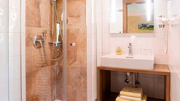 A modern bathroom with a glass-enclosed shower, a sink with a mirror above, and a wooden shelf with towels.