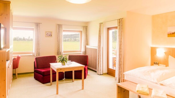 Quarto de hotel com uma cama, um sofá vermelho, uma mesa de madeira e uma janela com cortinas.