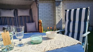 Una mesa dispuesta con una botella de eau de vie, dos copas, una vela y un cuenco sobre un mantel azul.