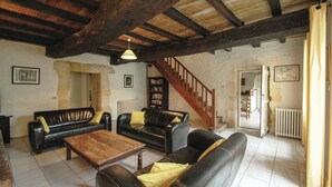 A rustic living room with exposed wooden beams, leather sofas, a wooden coffee table, and a staircase leading to another room.