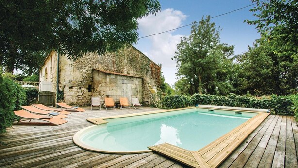 A wooden deck with a swimming pool, lounge chairs, and a stone building in the background.