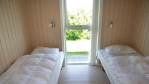 Ein Zimmer mit zwei Einzelbetten, Holzwänden, einem Fenster mit Blick auf Grünflächen und einer Tür.
