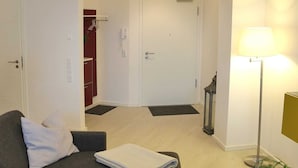 Ein Wohnzimmer mit einer Couch, einer Lampe und einer Tür, die zu einem Flur f ührt.