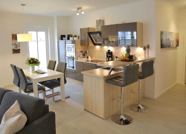 A modern kitchen with a central island, bar stools, and a dining area with a table and chairs.