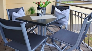 Ein Balkon mit Tisch und Stühlen, einer Weinflasche und einem Blumenstrauß.