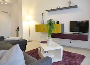 A modern living room with a grey sofa, a white coffee table, a potted plant, a TV, and a yellow accent wall.