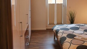 Ein Schlafzimmer mit Bett, Wand-Fernseher, Schiebetür und einer Pflanze.