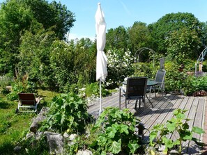 Een houten terras met een witte parasol, een metalen stoel en een tafel.