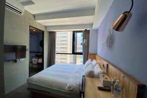 Ein Hotelzimmer mit Bett, Nachttisch, Lampe und Blick auf ein Gebäude durch das Fenster.