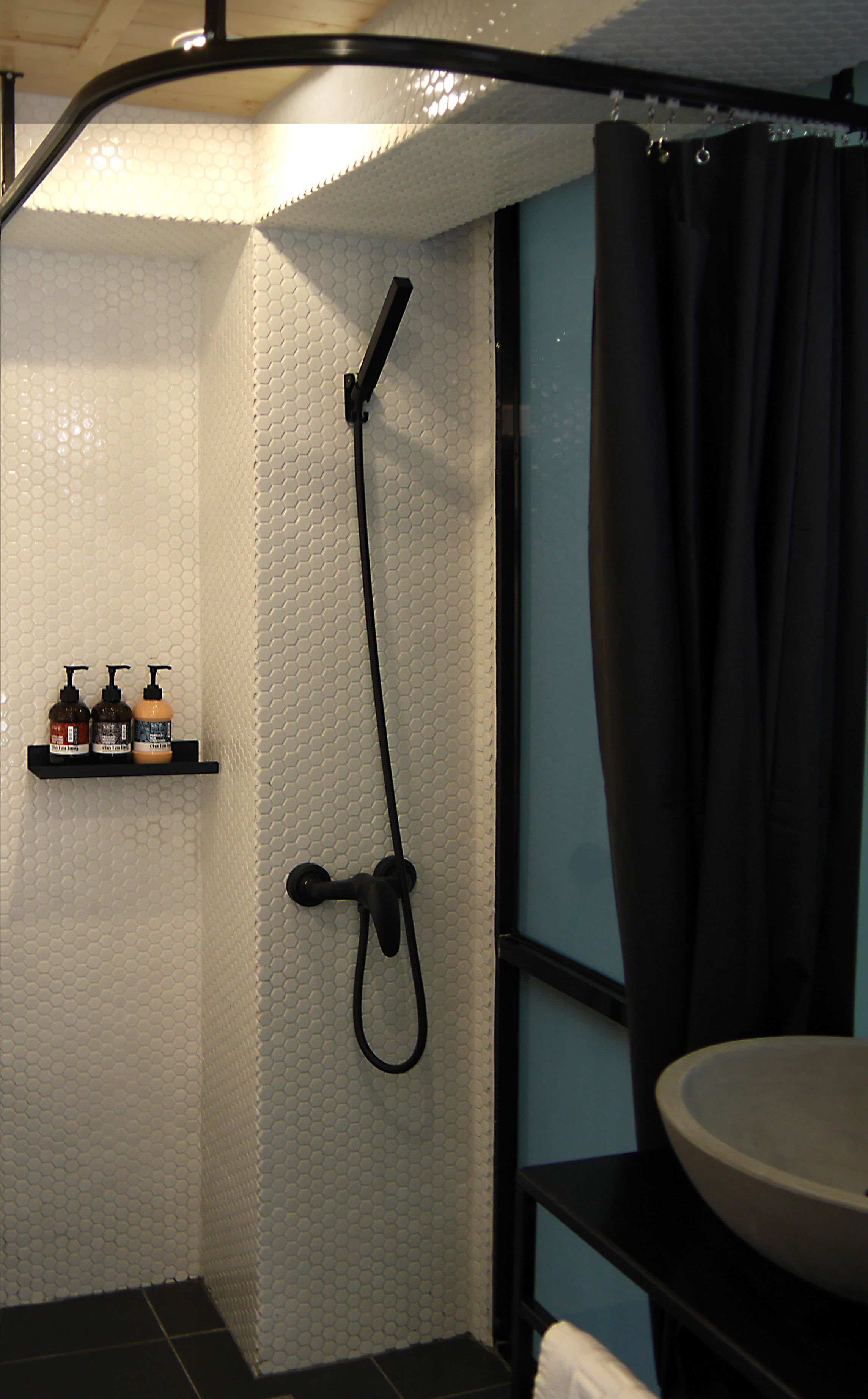 A bathroom with a shower, a sink, and a shelf with toiletries.