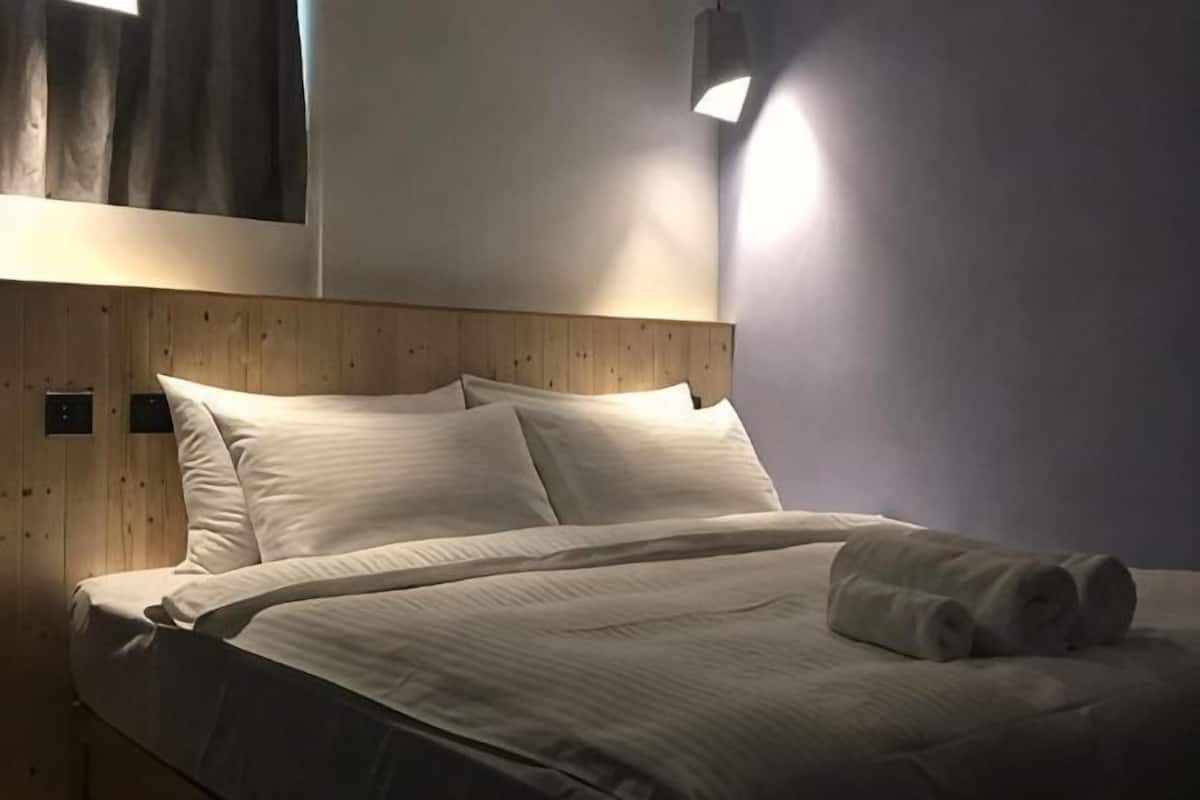 Ein ordentlich bezogenes Bett mit weißen Leinen und einem hölzernen Kopfteil, eine Wandleuchte und eine schlichte Wand.