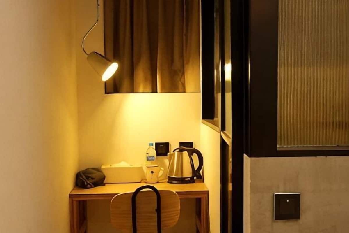 Ein kleiner Schreibtisch mit Stuhl, Lampe, Kaffeemaschine und einer Wasserflasche.
