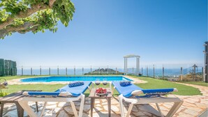 Een zwembadgedeelte met ligbedden en een tafel, met een helder uitzicht op zee, en een pergola.