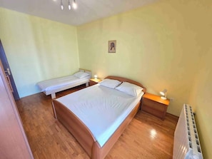 Une chambre avec deux lits simples et un lit double, un plancher en bois, un radiateur et un petit tableau accroché au mur.