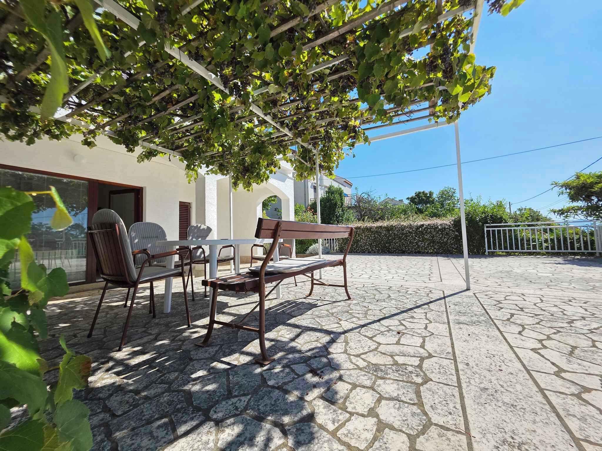 An outdoor patio with a table and chairs, a pergola with vines, and a stone floor.
