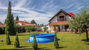 A residential area with a blue above-ground pool, neatly trimmed grass, and a house with a red roof. - Ferienhaus mit Außenpool und großem Garten (Balatonkeresztúr)