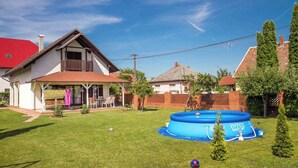 A residential backyard with a blue inflatable pool, a covered patio, and a red-roofed house. - Ferienhaus mit Außenpool und großem Garten (Balatonkeresztúr)