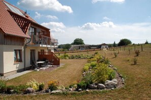 Ein zweistöckiges Haus mit einem Balkon, einer Terrasse mit Gartenmöbeln und einem gepflegten Garten.