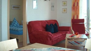 A room with a red sofa, a blue sofa, a wooden table, and a chair. There are two framed pictures on the wall. - Apartment Elly - House Uhleck (Lohme)