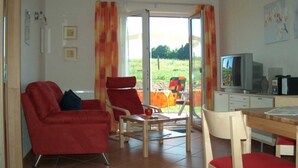 A living room with a red sofa, a wooden dining table, and a television. - Apartment Elly - House Uhleck (Lohme)