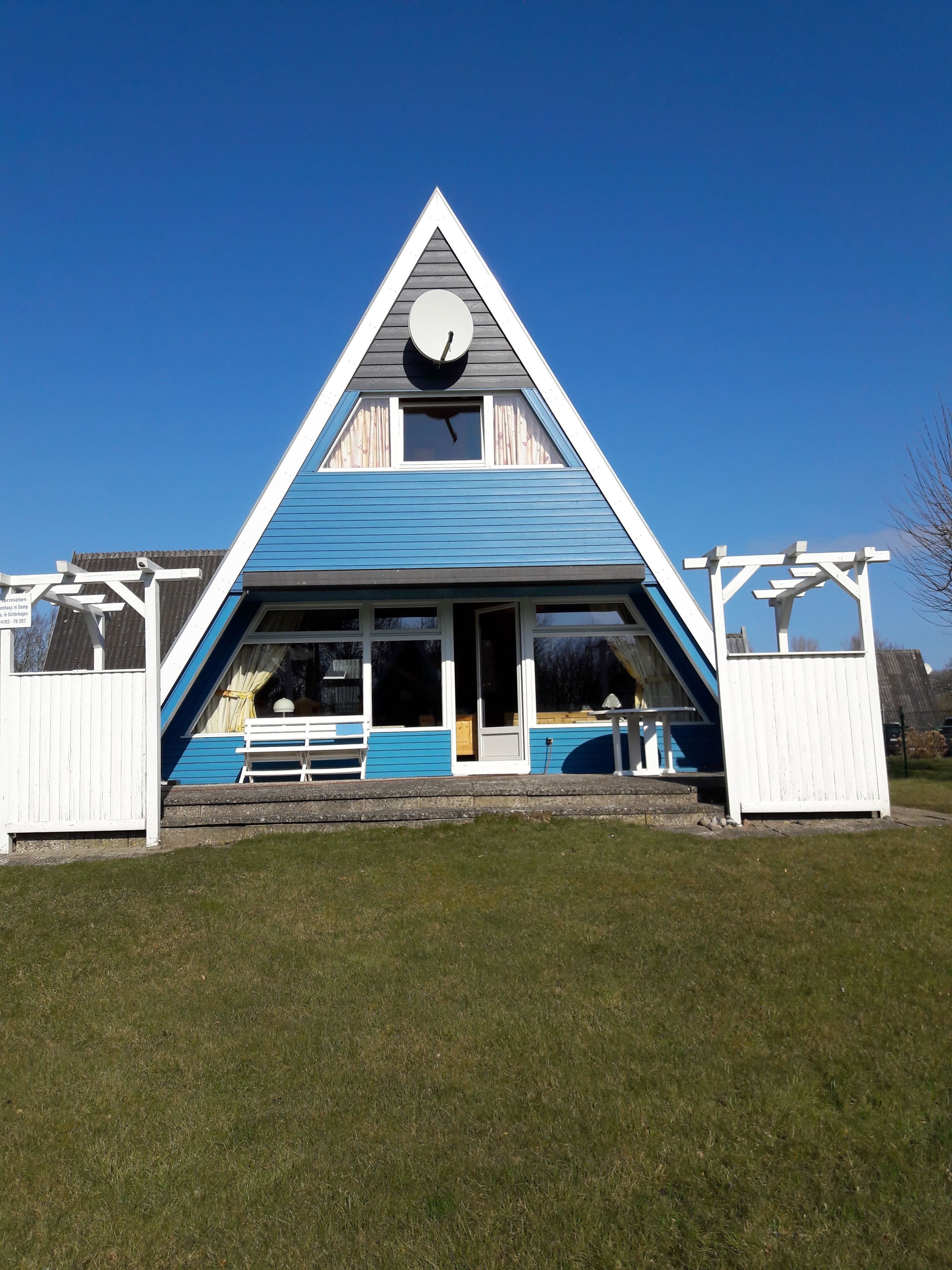 A triangular building with a clock, a bench, and a wooden fence.