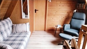Una habitación acogedora con un sofá a cuadros, una silla azul, una mesita y paredes de madera.