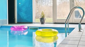 An indoor swimming pool with clear blue water, a metal ladder, and two inflatable rings, one pink and one yellow, on the pool floor. - Gorgeous home in Vejby with sauna (Vejby)