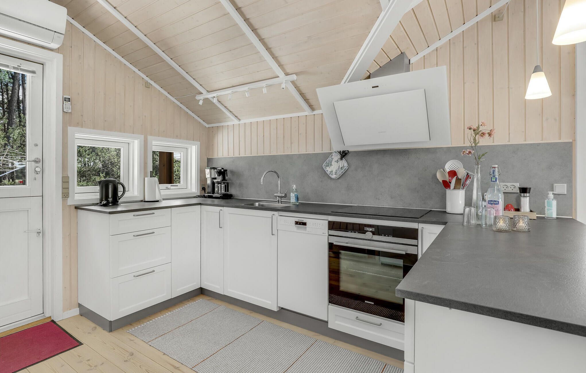 A modern kitchen with white cabinets, a built-in dishwasher, a coffee machine, and a large window.