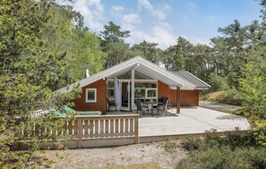 Situated in a forested area, this cabin features a large glass door leading to an outdoor seating area with a table and chairs.