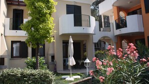 A courtyard with a tree, an umbrella, and a flower bed. - Holiday apartment with balcony and air conditioning (Bibione)
