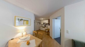 Un espace de vie compact comprenant un coin repas, une kitchenette et une porte donnant sur une autre pièce.