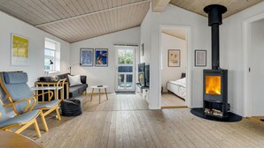 A cozy living room with a wooden ceiling, a black wood-burning stove, a sofa, chairs, and artwork on the walls. - 2 bedroom amazing home in Hjørring (Hjørring)