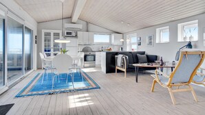 A modern kitchen with white cabinets, a dining area with a white table and chairs, a sofa, and a blue rug. - 2 bedroom amazing home in Hjørring (Hjørring)