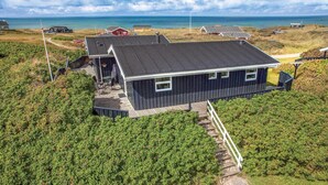 A coastal house with a dark roof, a covered patio, and a view of the sea. - 2 bedroom amazing home in Hjørring (Hjørring)