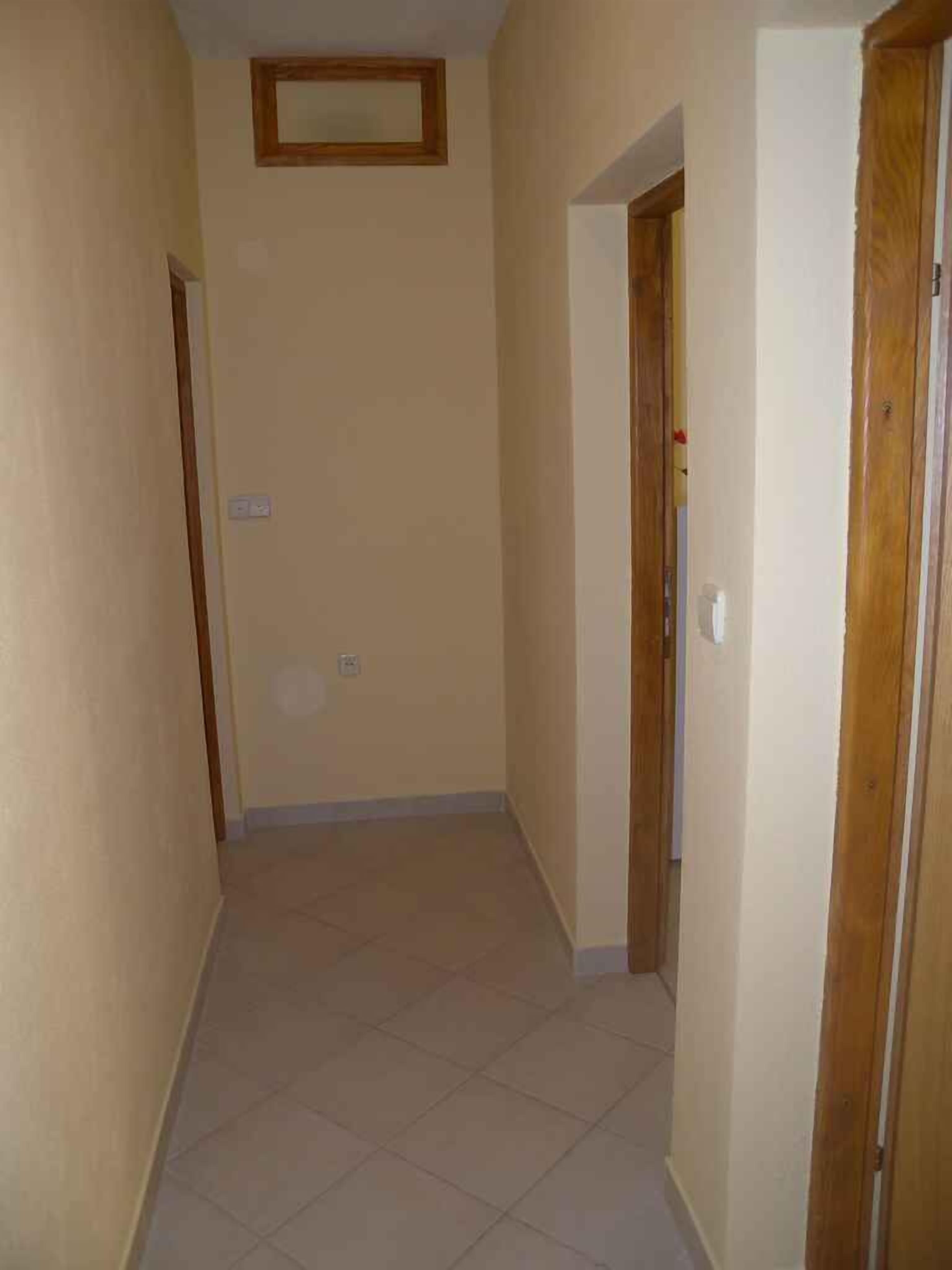 A narrow hallway with tiled flooring and beige walls.
