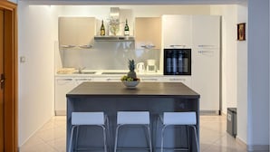 A modern kitchen with white cabinets, a central island with a bowl of fruit, and three bar stools. - Cozy home in Buje with private swimming pool, can be inside or outside (Buje)