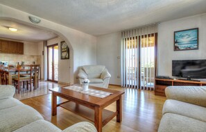 Relax in this inviting living area with a coffee table, armchairs, and a TV, surrounded by a large window and a kitchen area.