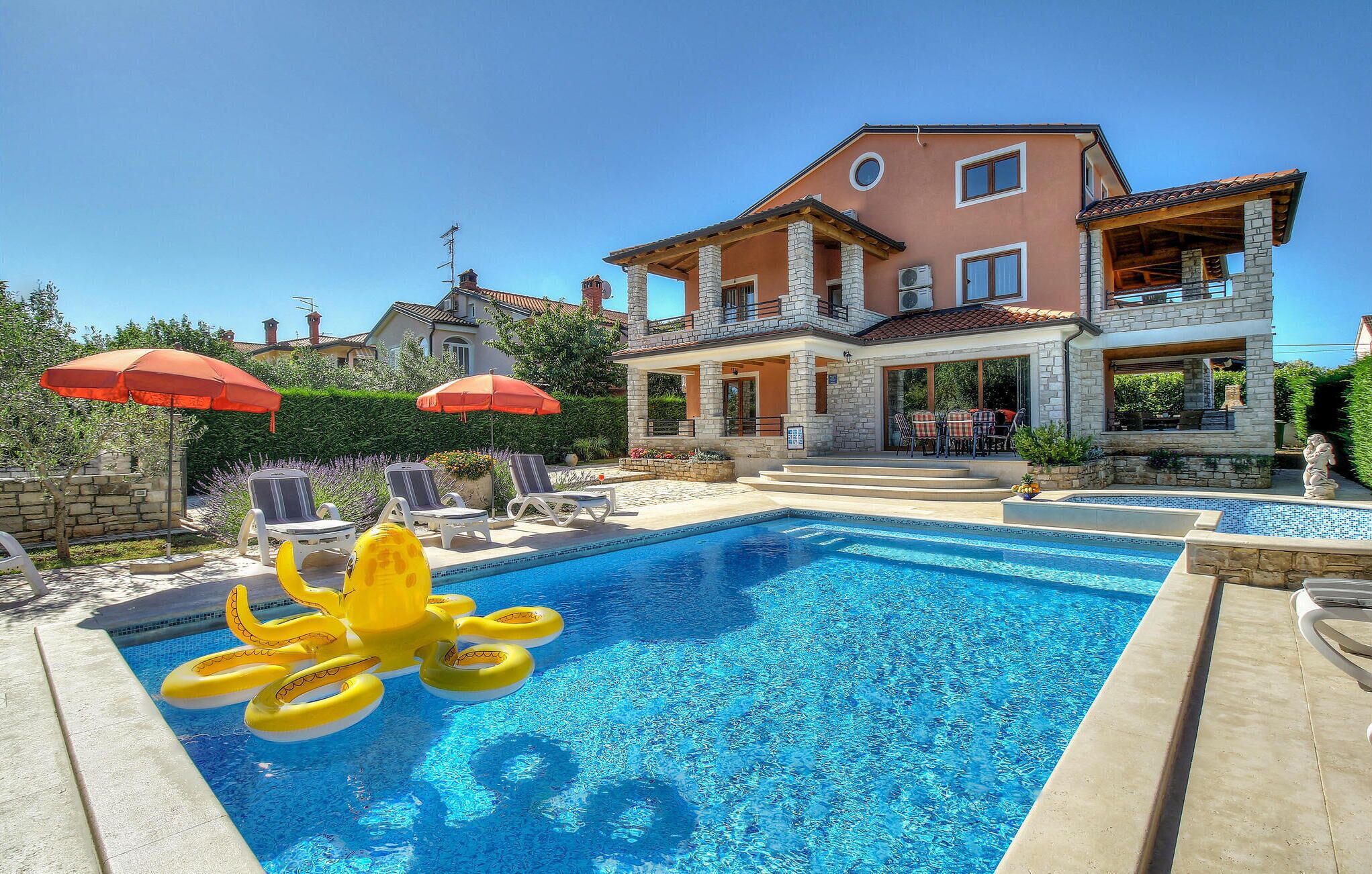 A swimming pool with inflatable rings, a covered patio, and a two-story house with stone facade and multiple windows.