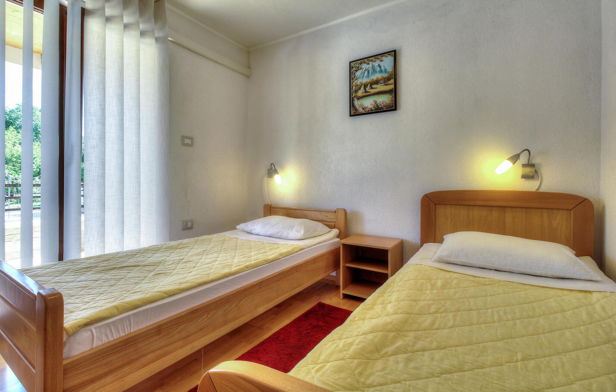 A room with two wooden beds, a red rug, and a painting on the wall.