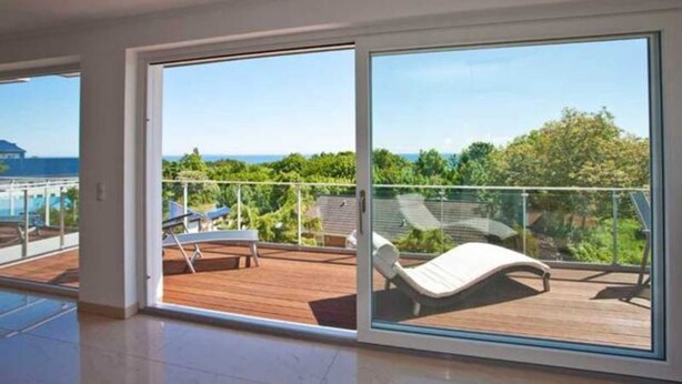 Un vaste balcon doté d’une terrasse en bois, d’un fauteuil de relaxation et offrant une vue sur la verdure et un bâtiment situé au loin.