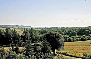 Un paysage rural avec des champs, des arbres et une étendue d’eau visible au loin, sous un ciel dégagé.