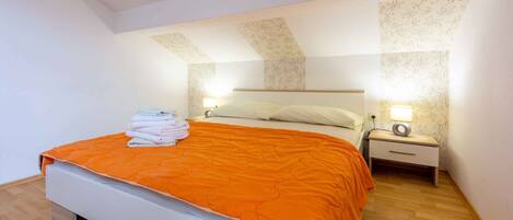 A bedroom with a bed, two bedside tables, a nightstand, and a wall-mounted lamp.