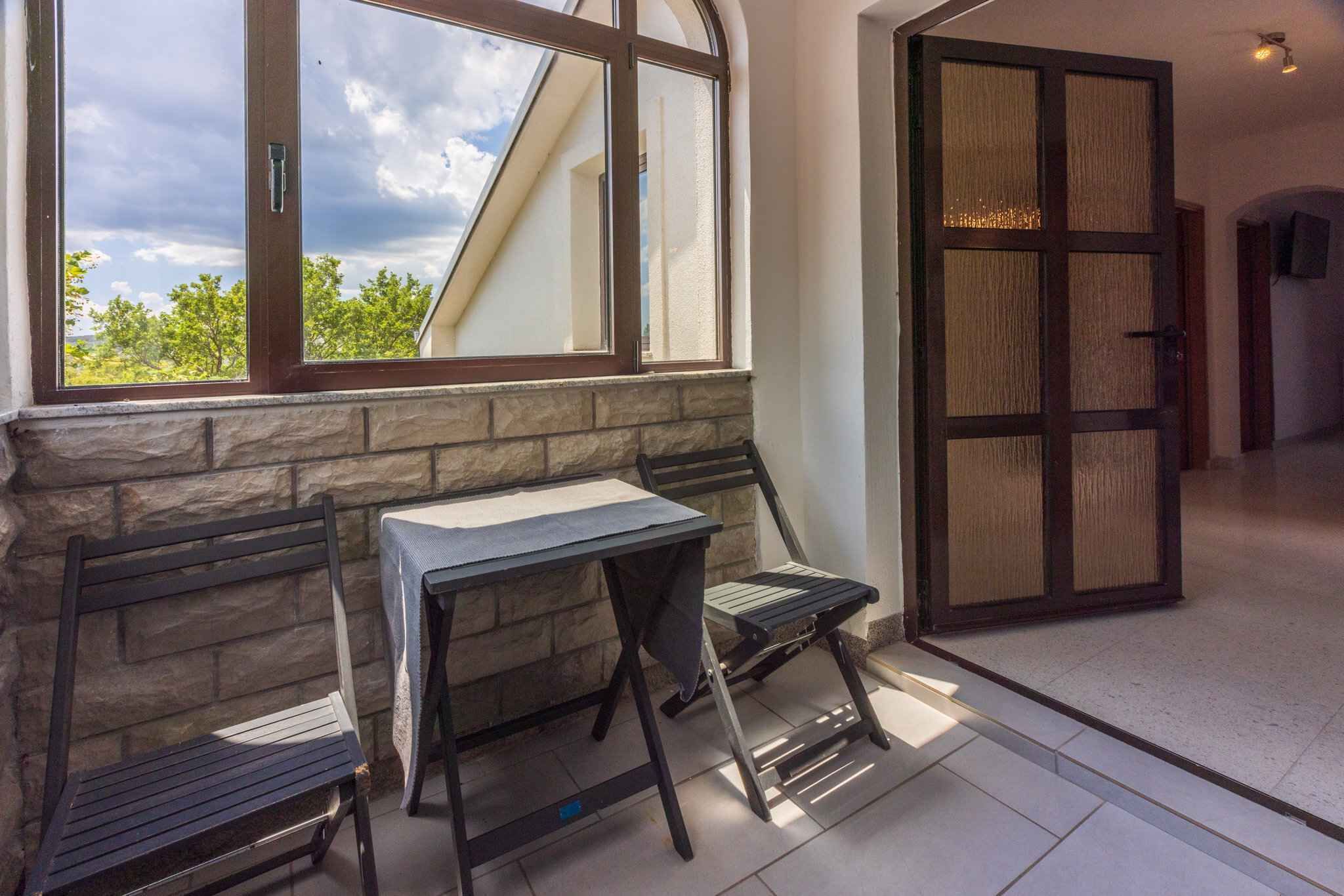 A room with a stone wall, a table with a tablecloth, two chairs, and a large wooden door.