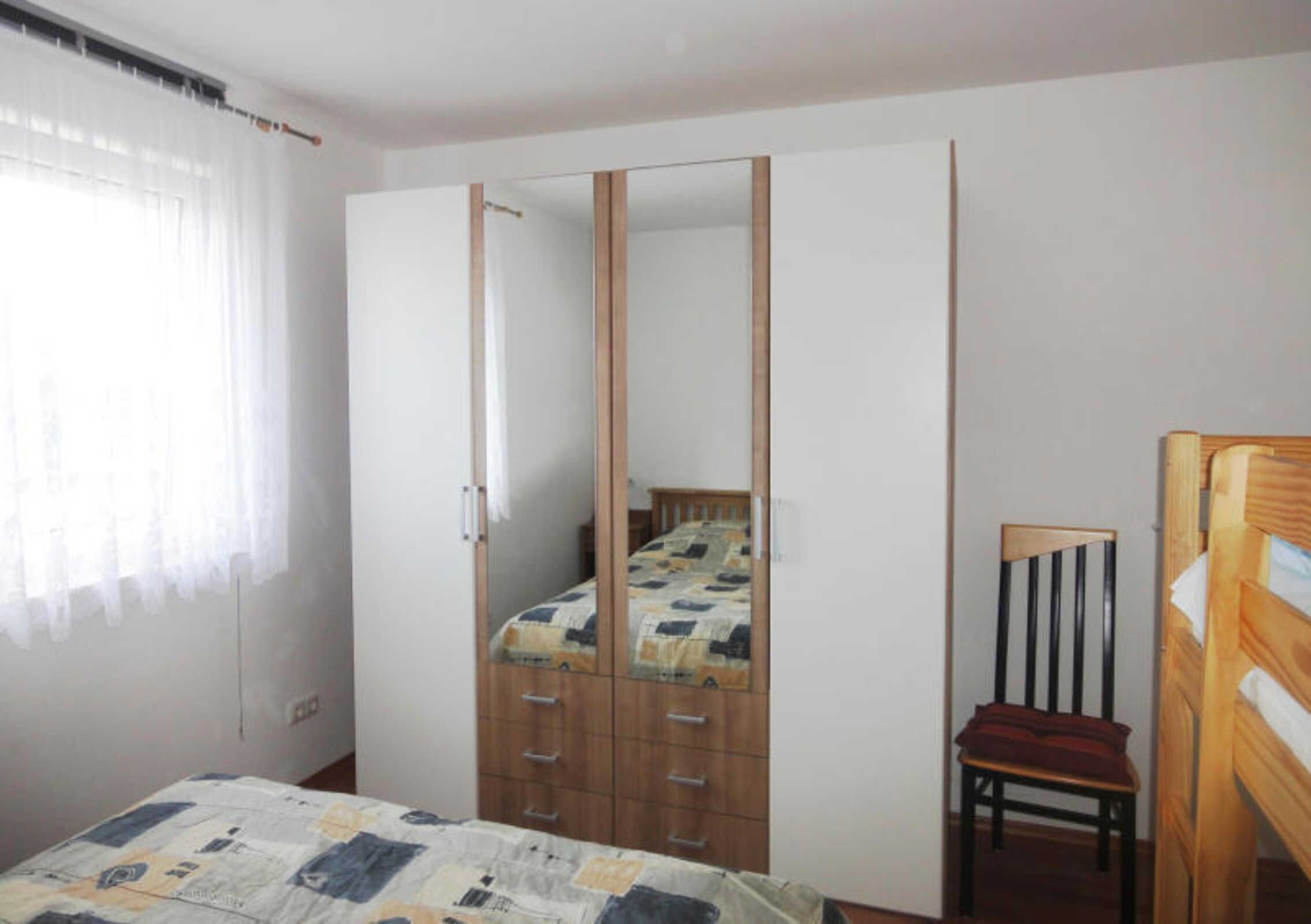 Une chambre à coucher avec un lit, une armoire, une chaise et un miroir.