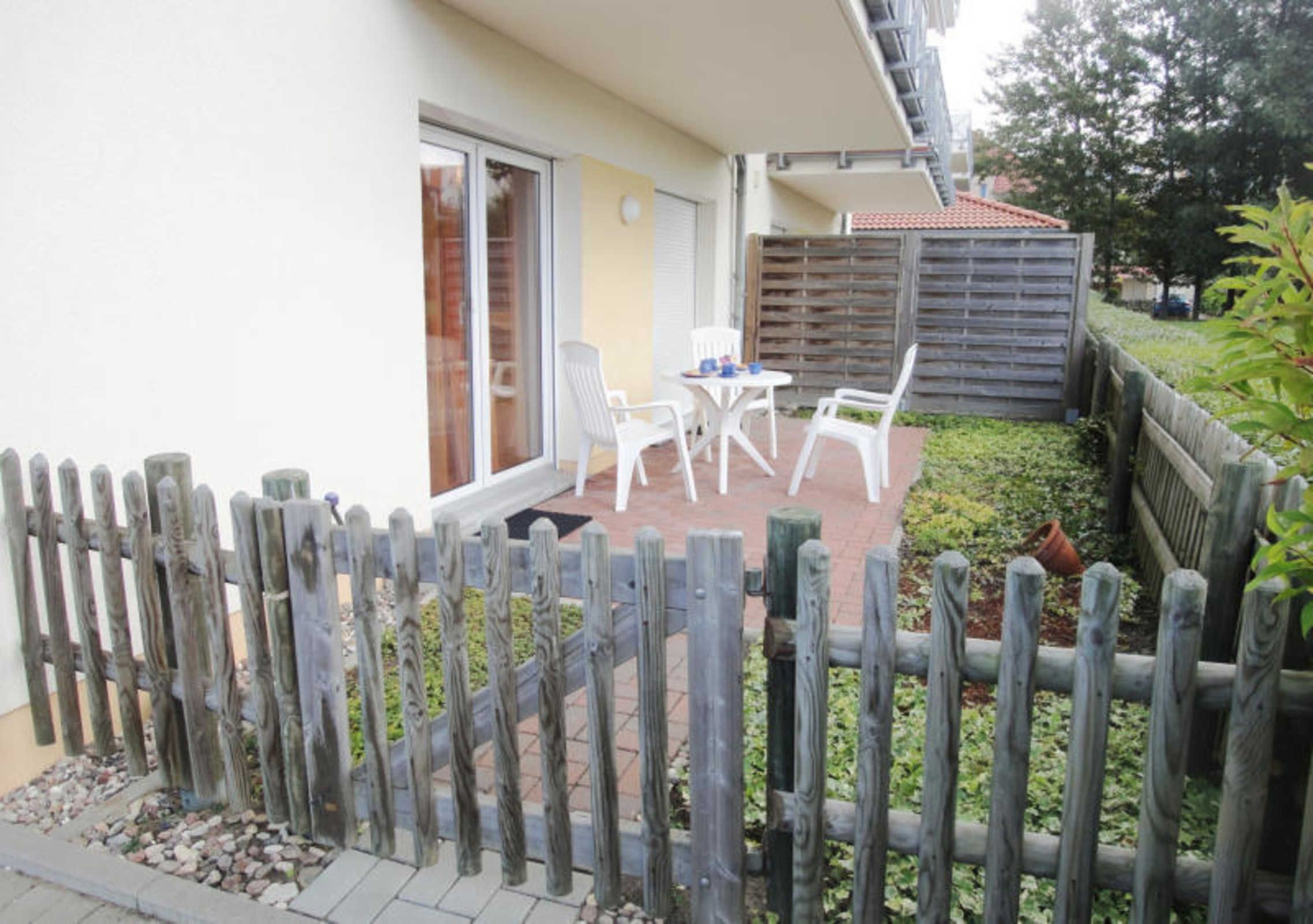 A patio with a table and chairs, a wooden fence, and a building with a tiled roof.