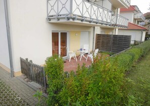 Un edificio residenziale con un balcone, un patio con sedie e una recinzione in legno.