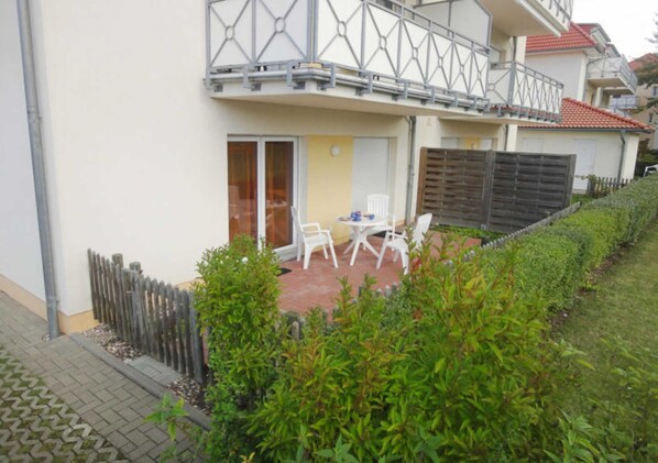 A residential building with a balcony, a patio with chairs, and a wooden fence.