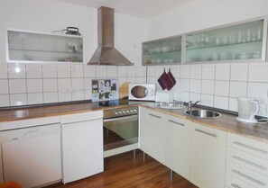 Eine Küche mit weißen Schränken, einem Geschirrspüler, einem Backofen, einer Mikrowelle, einem Spülbecken und einem Wasserkocher.