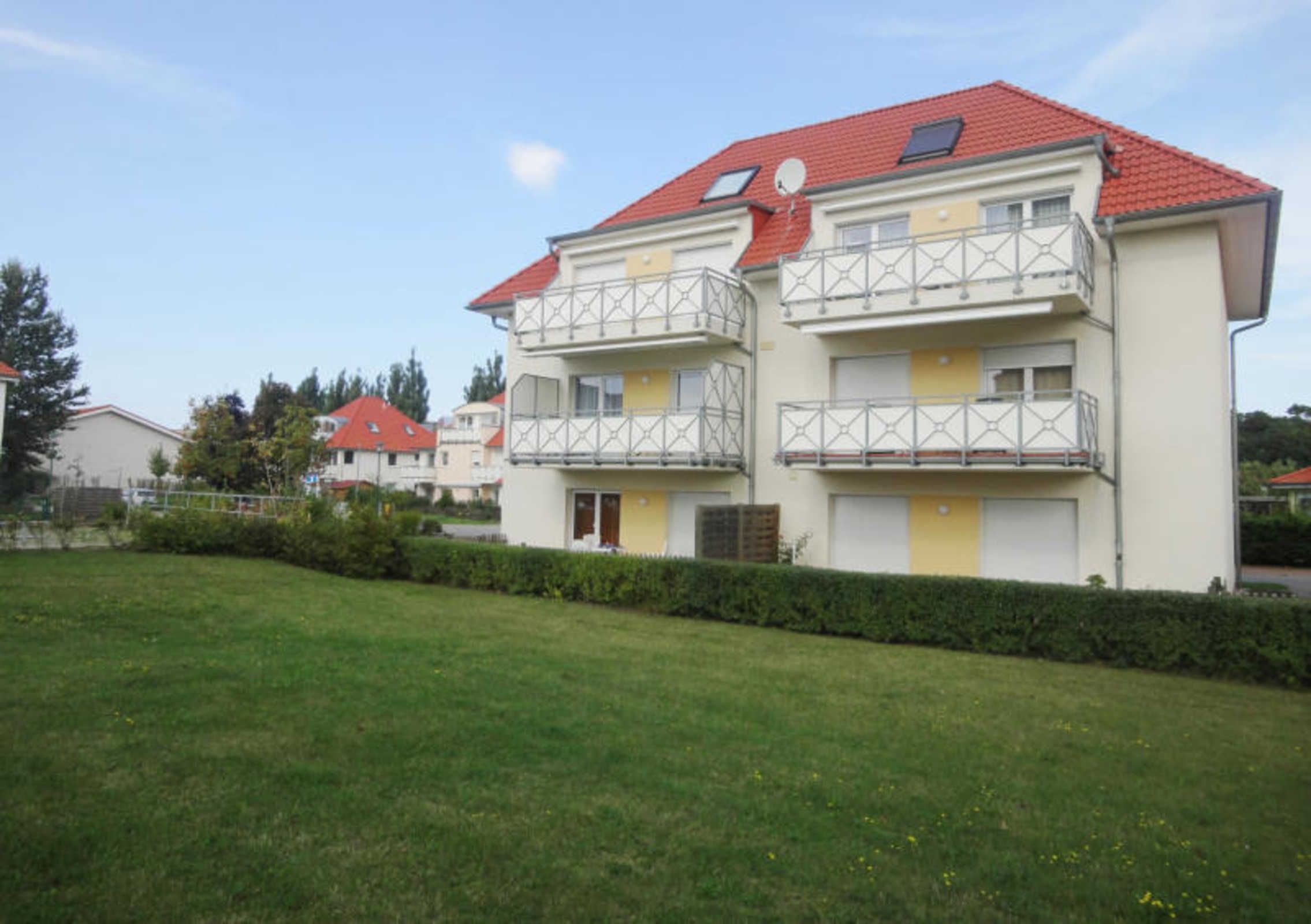 A multi-story residential building with balconies, a red roof, and a well-maintained lawn.