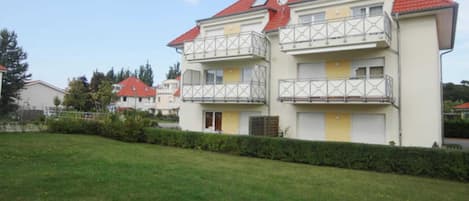 A multi-story residential building with balconies, a red roof, and a well-maintained lawn.